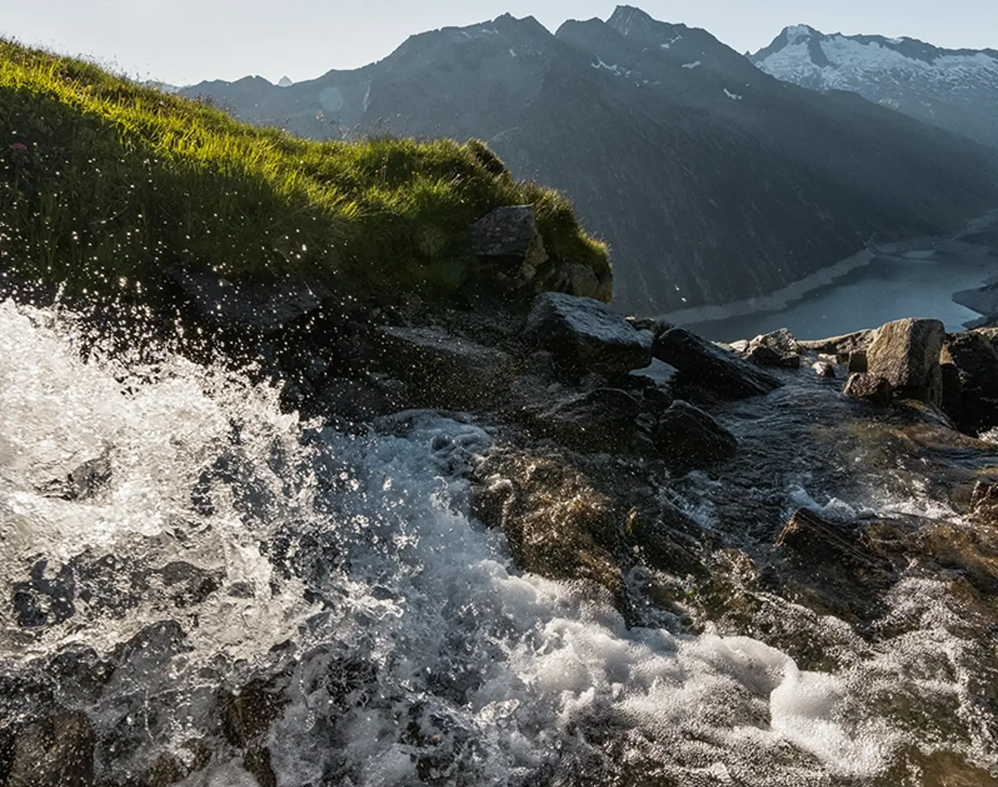 Ein Bergbach bahnt sich seinen Weg in die Tiefe. Die Sonne strahl und der Himmel ist blau.