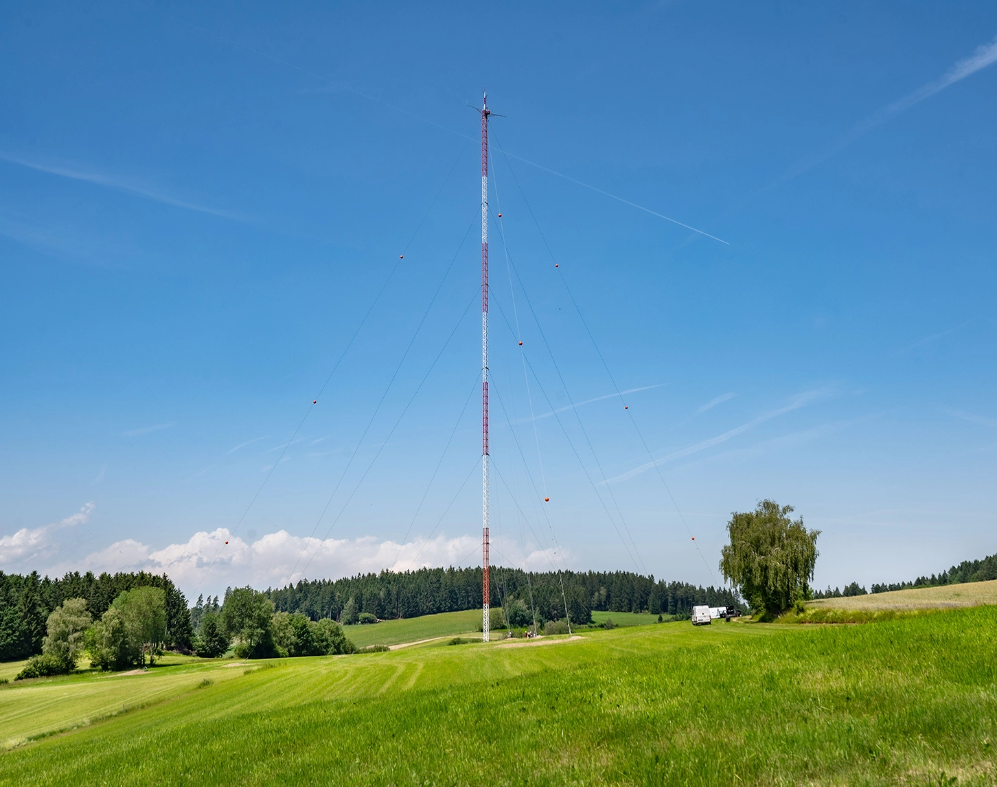 Das Bild zeigt den Wendmess-Mast, der am Schiffberg ökologische Informationen sammelt. Das Wetter ist herrlich sonnig und die Wiesen sind grün.