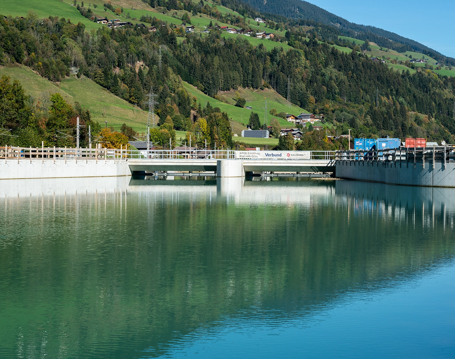 Wir blicken auf eine Brücke beim Kraftwerk Gries. Die Umgebung ist ländlich und die Sonne scheint.