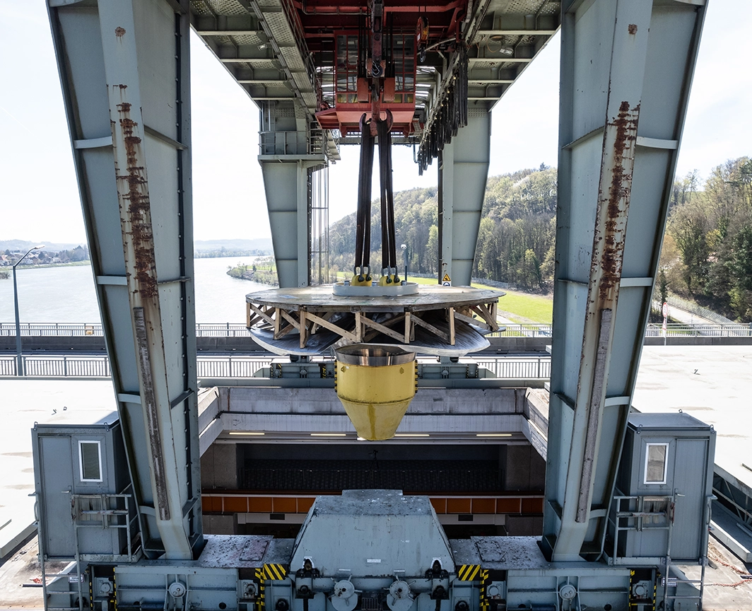 Wir sehen wie eine neue Turbine via Kran ins Innere eines Kraftwerks abgeseilt wird.