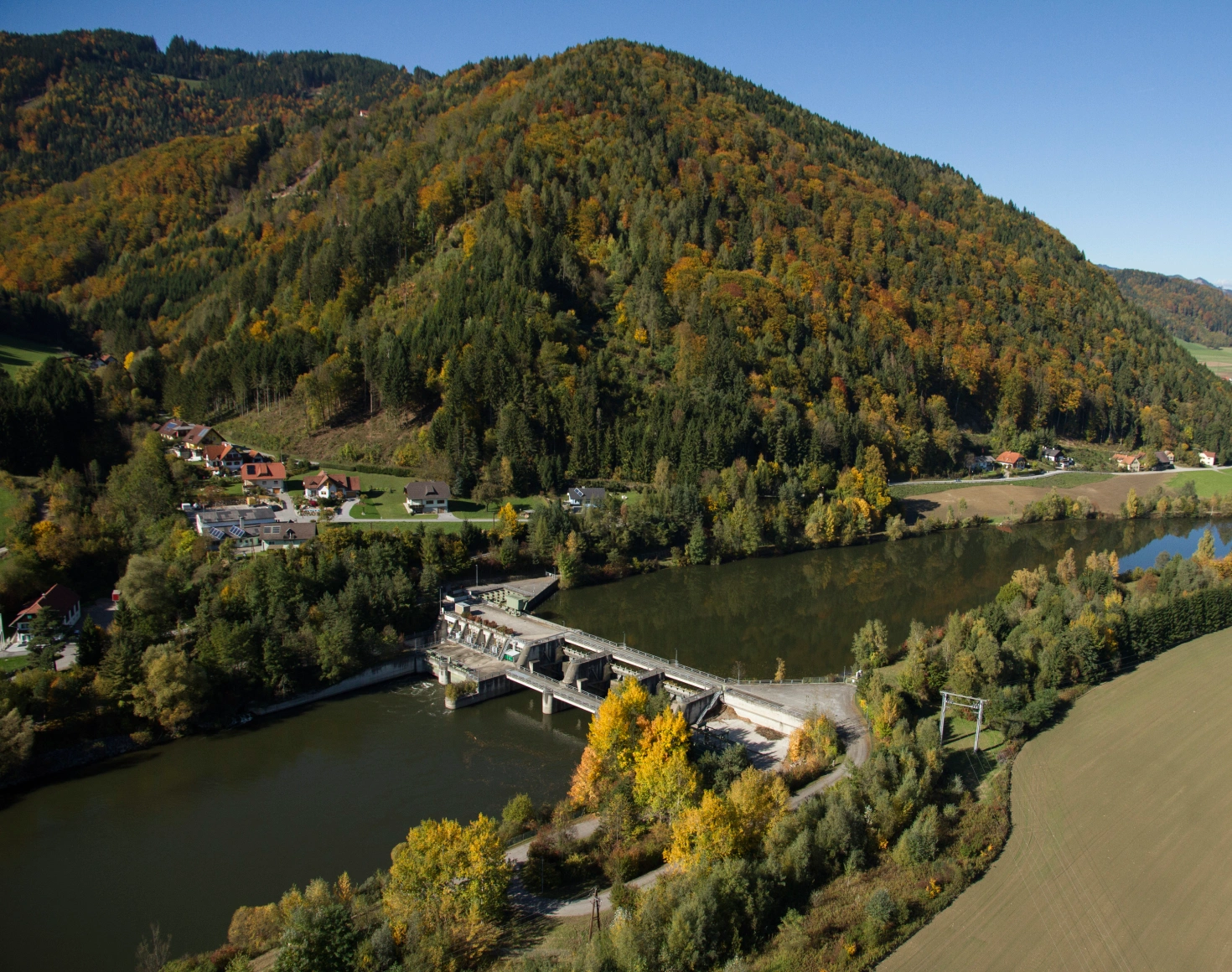 Ein Blick von oben auf das Kraftwerk Rabenstein im Herbst. Die Sonne scheint und der Wald zeigt sich abwechslungsreich im Jahreszeitenwandel.
